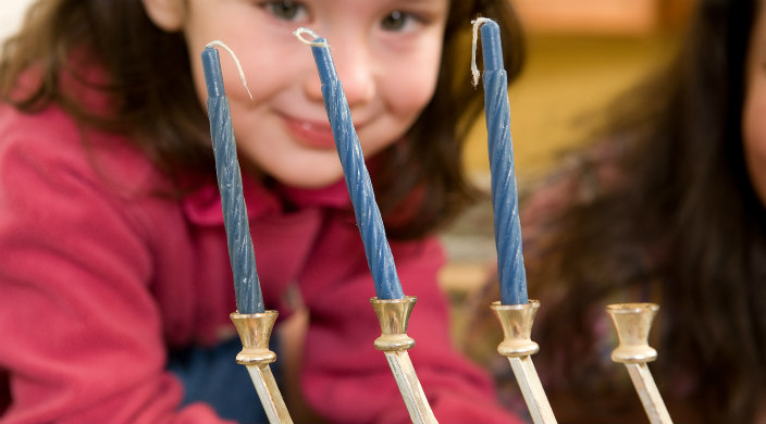 Preschooler looking at hanukkiyah with unlit candles in it
